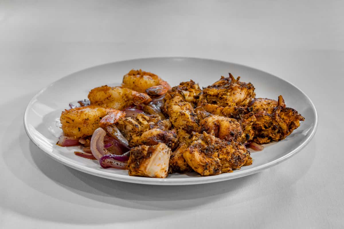 Plate of Cajun-style grilled shrimp and blackened chicken served with sautéed red onions, seasoned with bold spices for a Southern-inspired entrée.