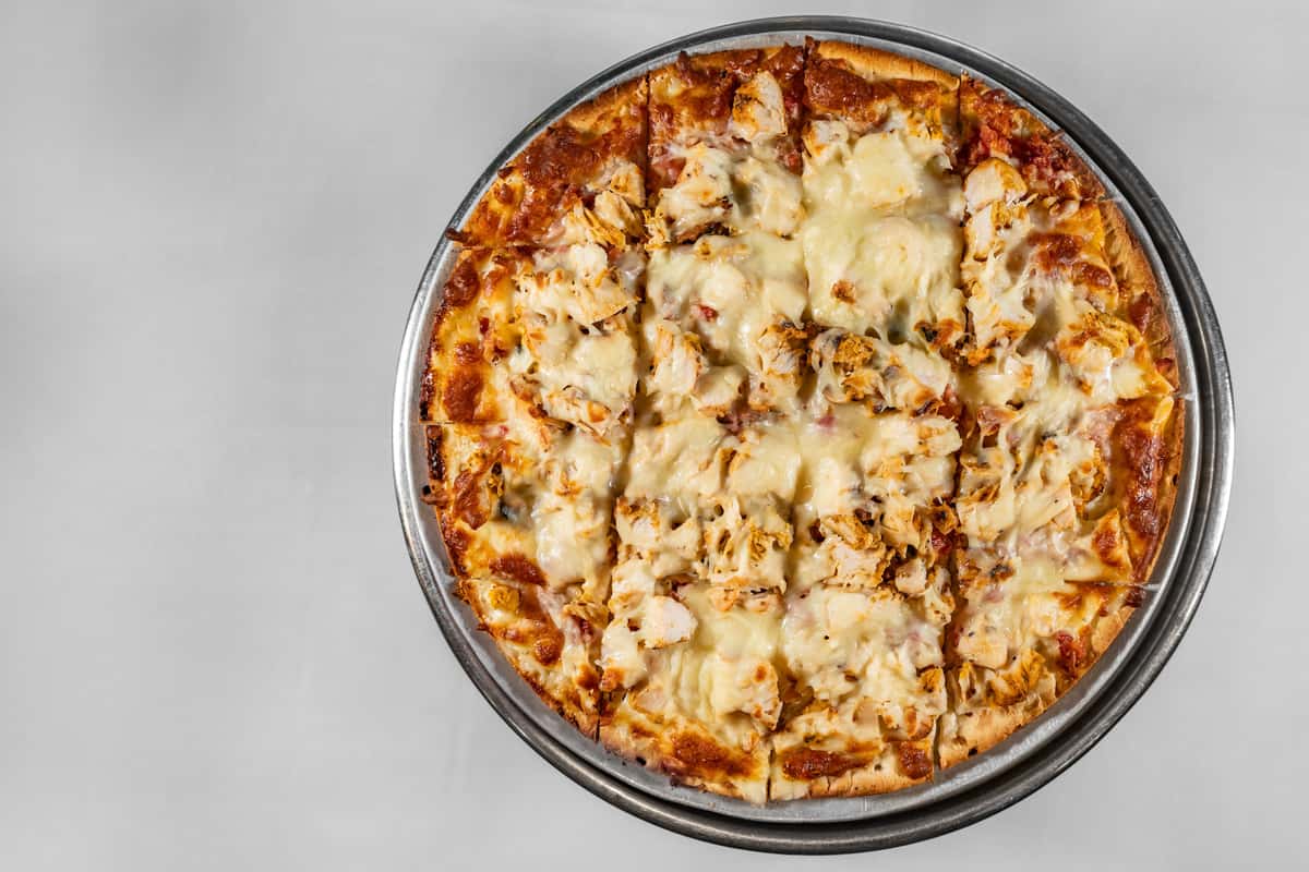 Overhead view of a hand-tossed chicken pizza topped with melted mozzarella cheese and grilled chicken chunks on a golden-brown crust, served on a metal tray.