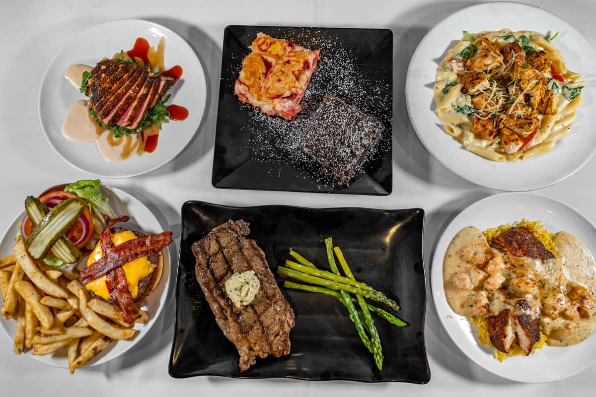 "Top-down view of an assorted American restaurant entrée spread including seared ahi tuna over greens with sauce, creamy chicken Alfredo pasta, blackened fish with shrimp in a Cajun cream sauce over rice, grilled ribeye steak with garlic herb butter and asparagus, a bacon cheeseburger with fries and fresh toppings, and a dessert plate featuring a chocolate brownie and a fruit cobbler dusted with powdered sugar.