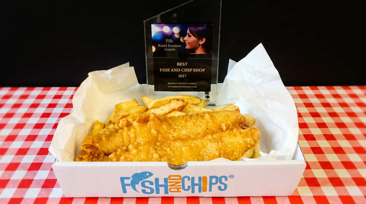 Fish and chips in a white takeaway box, with an award for "Best Fish and Chip Shop 2017" behind it.