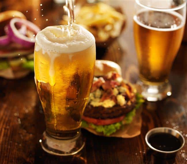 beer being poured into a glass, with a cheeseburger and another beer in a glass on a table
