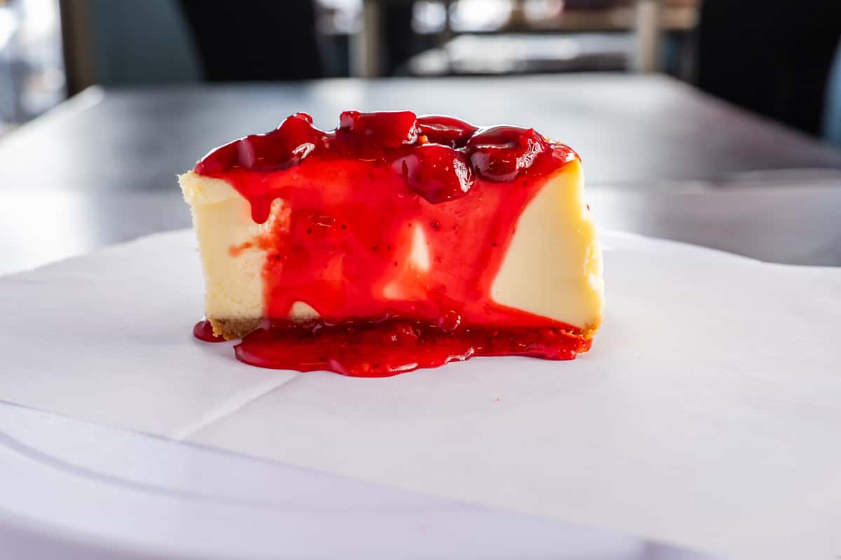 creamy cheesecake slice topped with glossy strawberry sauce and fresh berries, served as a classic dessert in restaurant setting