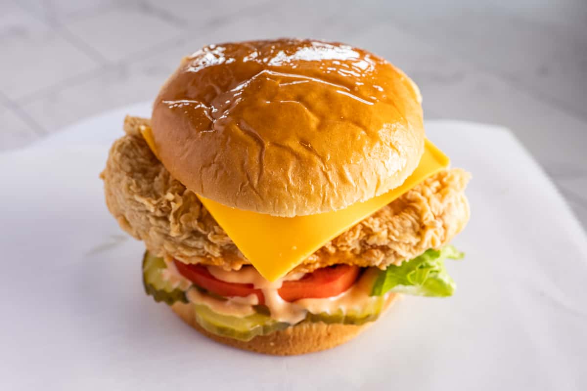 crispy fried chicken sandwich with cheddar cheese, lettuce, tomato, and pickles on a toasted bun