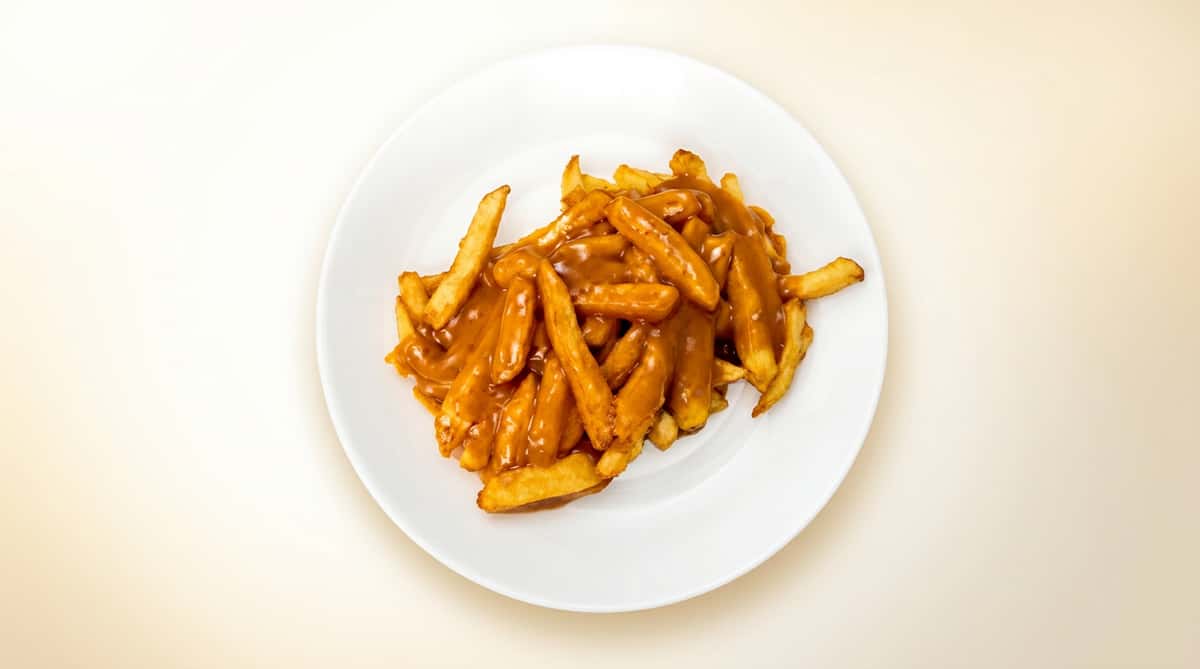 Poutine: French fries topped with gravy on a white plate.