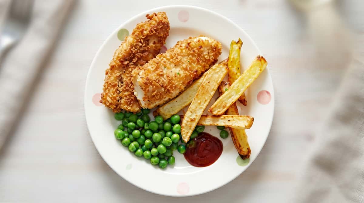 Fish and chips meal with two breaded fish sticks, french fries, peas, and ketchup on a white plate.