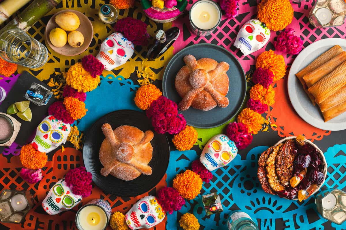 Colorful Día de los Muertos altar with pan de muerto, tamales, sugar skulls, marigolds, candles, and traditional decorations.