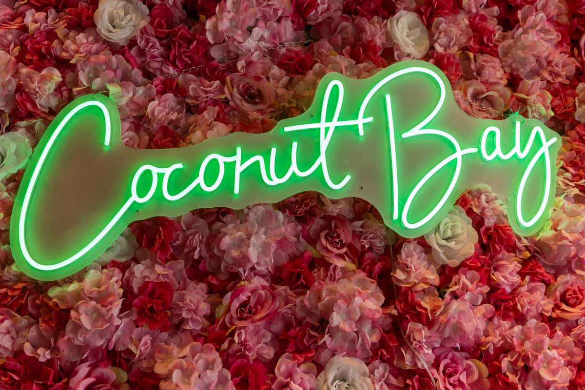 A vibrant floral wall with glowing neon signage creates a stylish and modern backdrop, adding a lively and Instagram-worthy touch to the dining atmosphere.