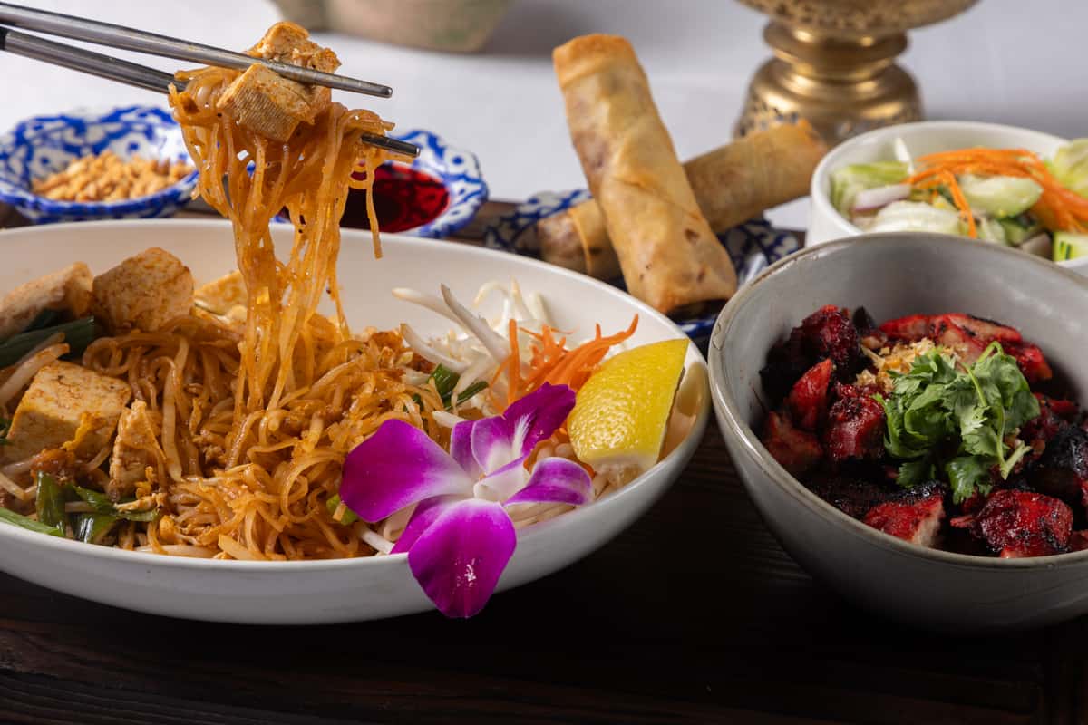 Authentic Pad Thai stir-fried with flavorful noodles, fresh vegetables, and savory Thai sauce, served with crispy spring rolls and vibrant traditional sides for a bold and satisfying dining experience.
