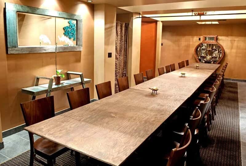 private dining room with long wooden communal table, warm lighting, and minimalist Thai-inspired decor for group dining experience