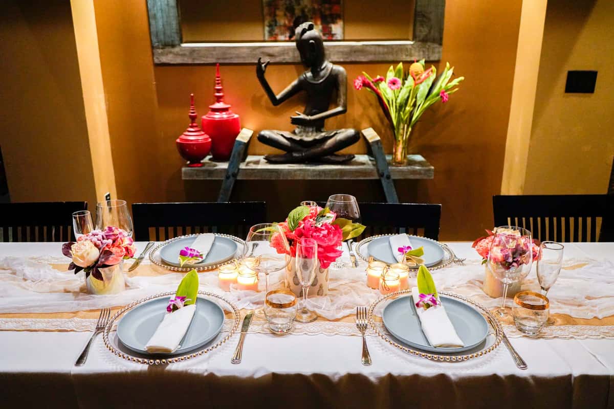 elegant restaurant dining table with floral centerpieces, candles, and Thai-inspired decor featuring a serene statue backdrop