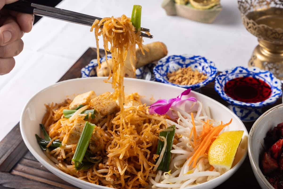 Stir-fried Thai noodles tossed with fresh vegetables, tofu, and savory house-made sauce, garnished with herbs and served with fresh lime and cabbage for a vibrant, authentic Thai flavor.