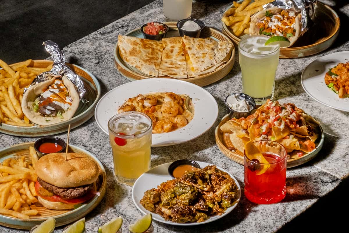 Full table spread of Mediterranean dishes, pizza, pasta, burgers, and cocktails at Sivas Tavern