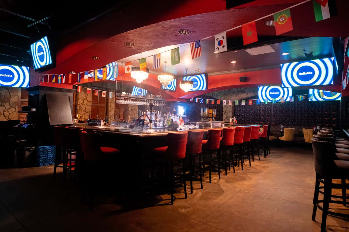 Lively bar area at Sivas Tavern with red ambient lighting, bar stools, and TV screens