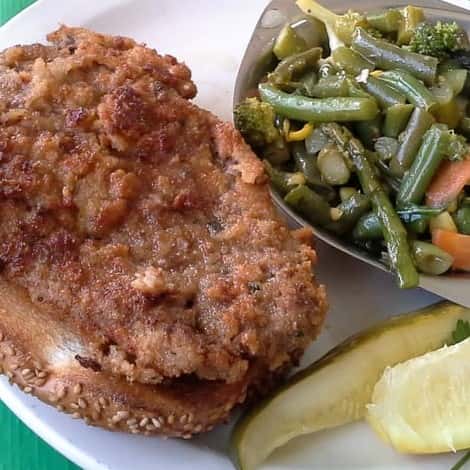 fried pork chop on a piece of bread with a side of green beans and a pickle