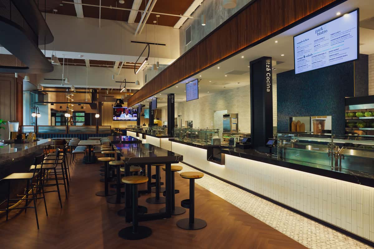 A spacious and modern event space in Dallas, TX featuring a long bar with stools, multiple high-top tables with chairs,