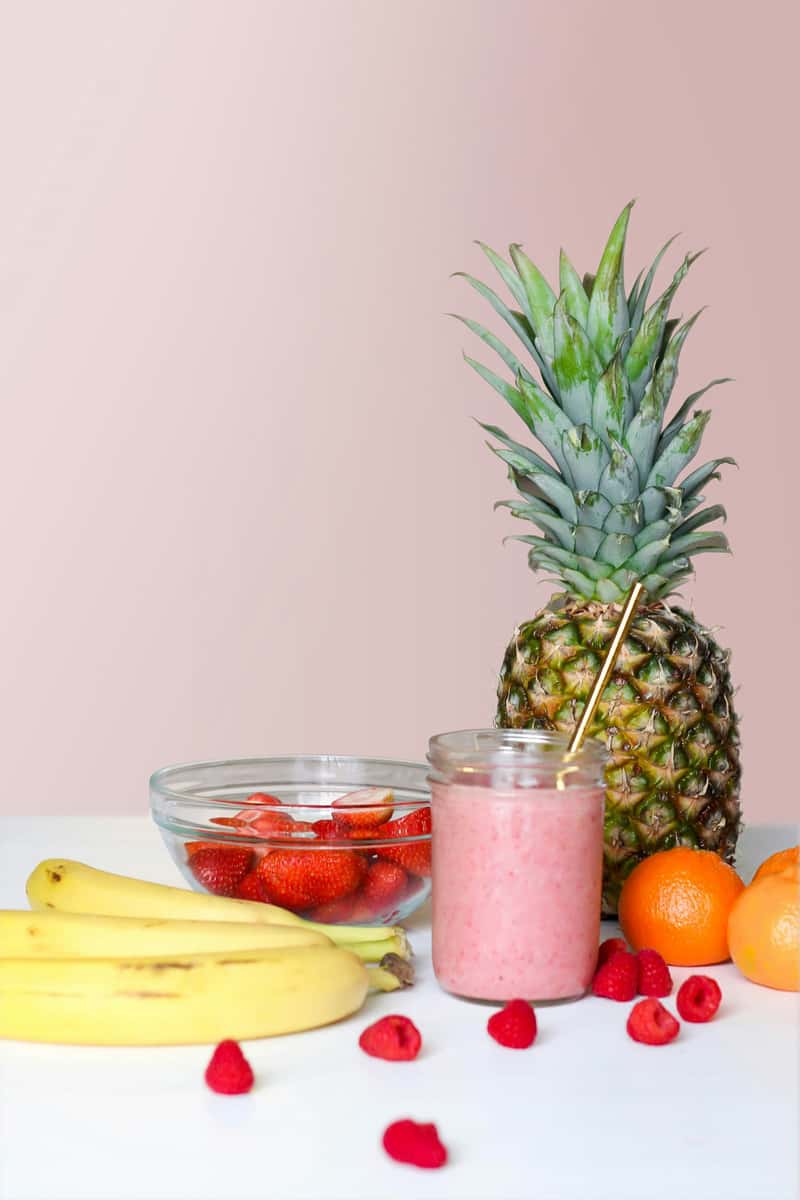 Photo of a smoothie next to pineapple, bananas, and other fruit.
