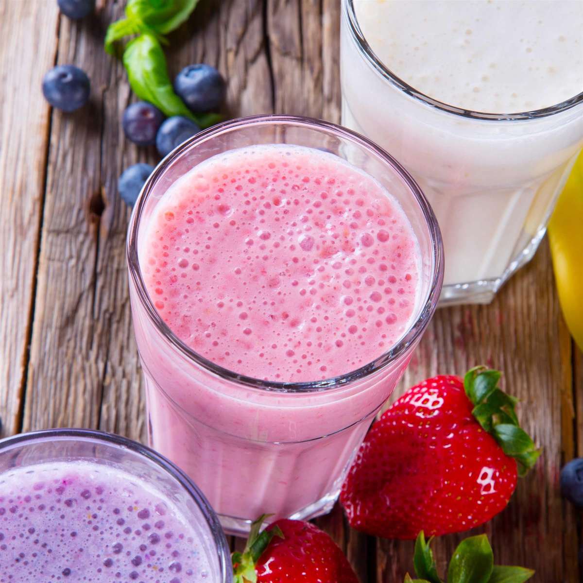 Fresh milk, strawberry, blueberry and banana drinks on wodeen table, assorted protein cocktails with fresh fruits.