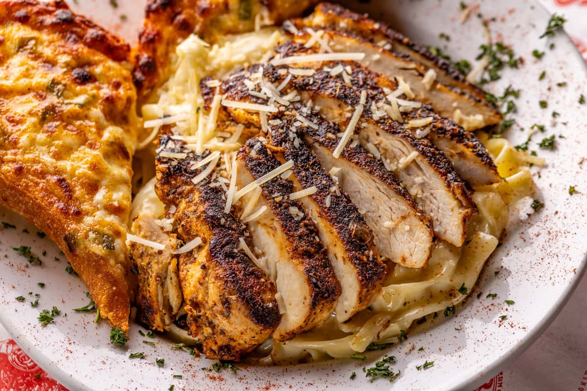 Blackened grilled chicken over creamy Alfredo pasta topped with parmesan cheese and served with cheesy garlic bread