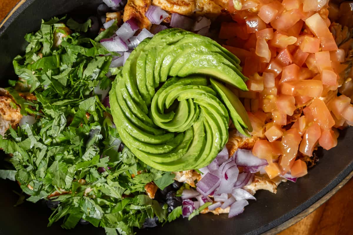 Chicken bowl topped with diced tomatoes, red onions, cilantro, and a decorative spiral of sliced avocado.