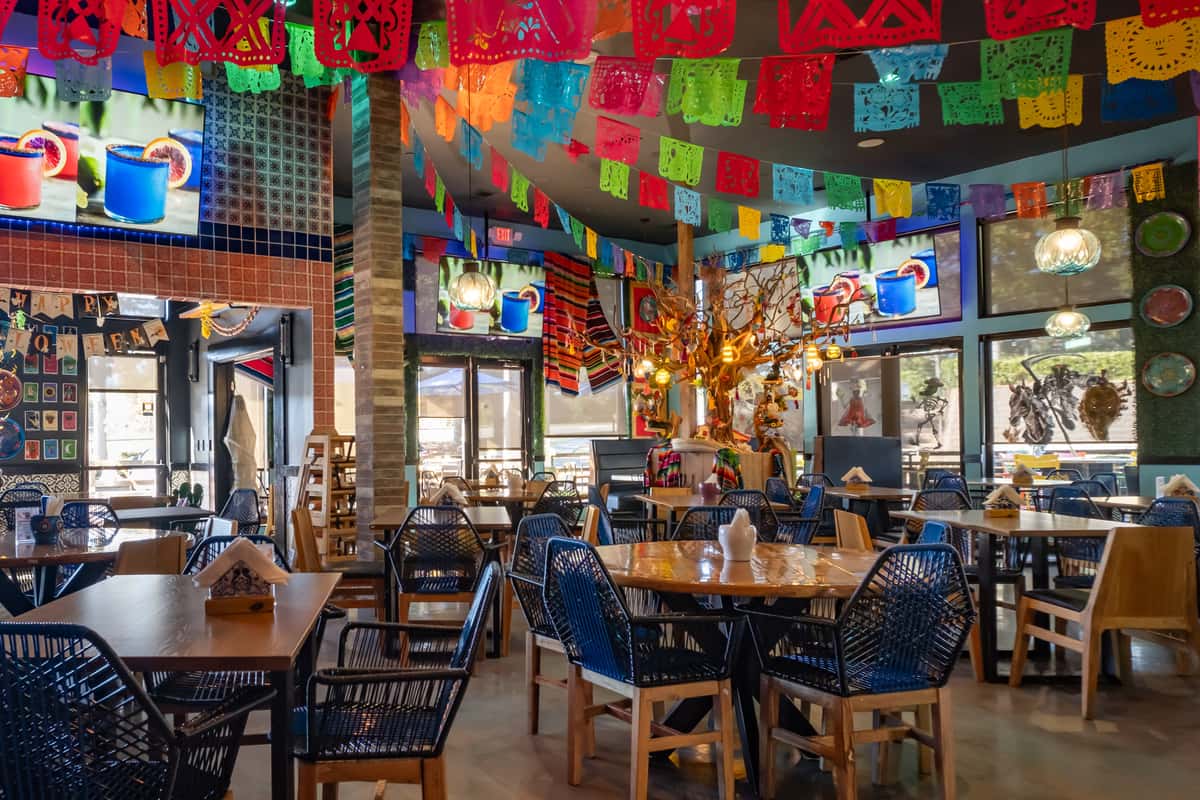Vibrant Mexican restaurant interior with papel picado banners, sombreros, colorful blankets, and festive wooden décor.