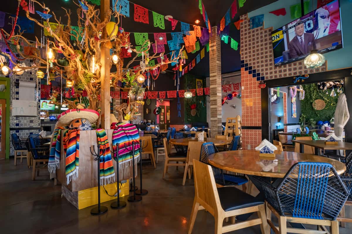 Vibrant Mexican restaurant interior with papel picado banners, sombreros, colorful blankets, and festive wooden décor.