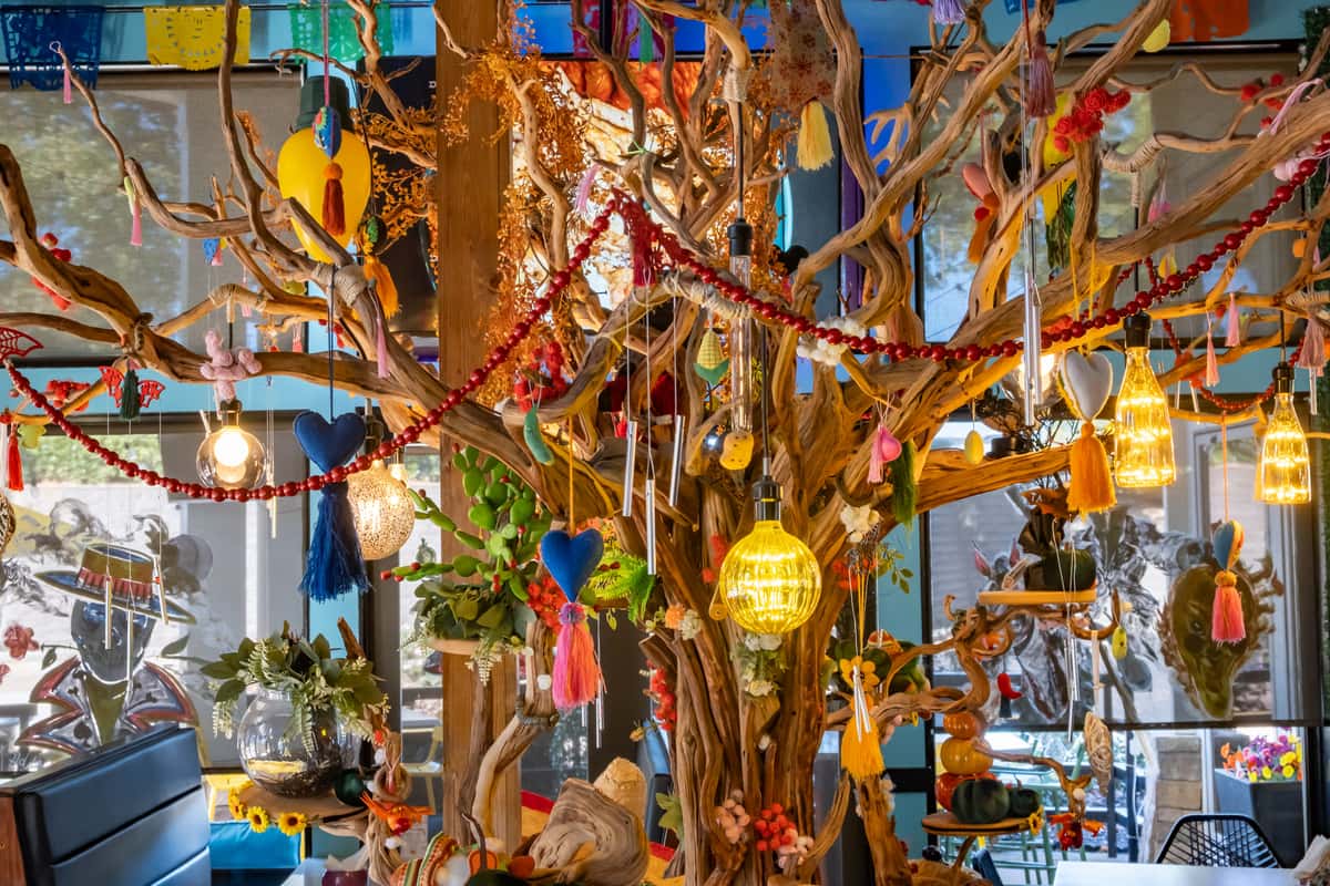 Decorative wooden tree adorned with colorful hanging ornaments, tassels, and glowing pendant lights in a festive setting.