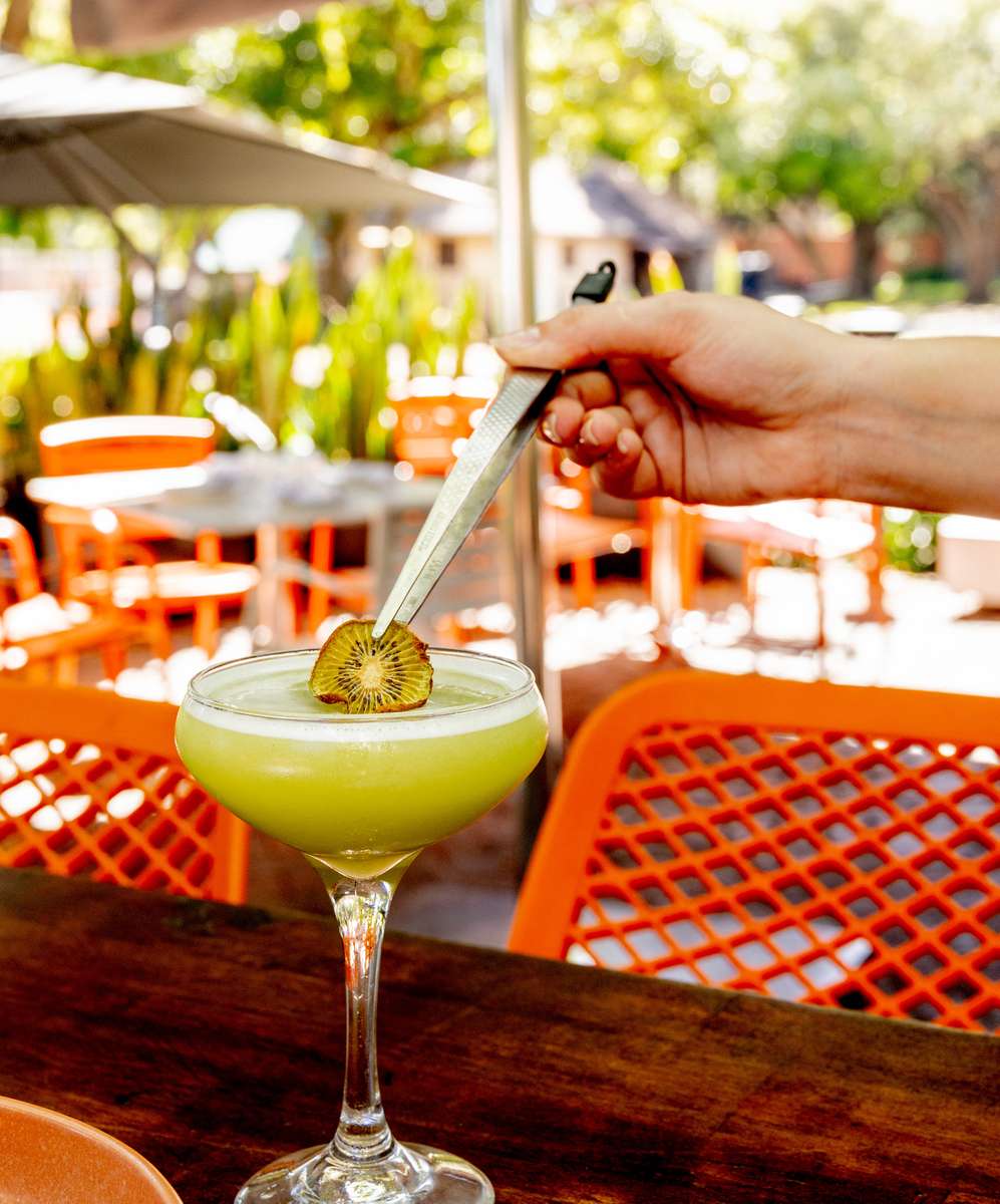 Green cocktail with kiwi garnish served at an outdoor restaurant.