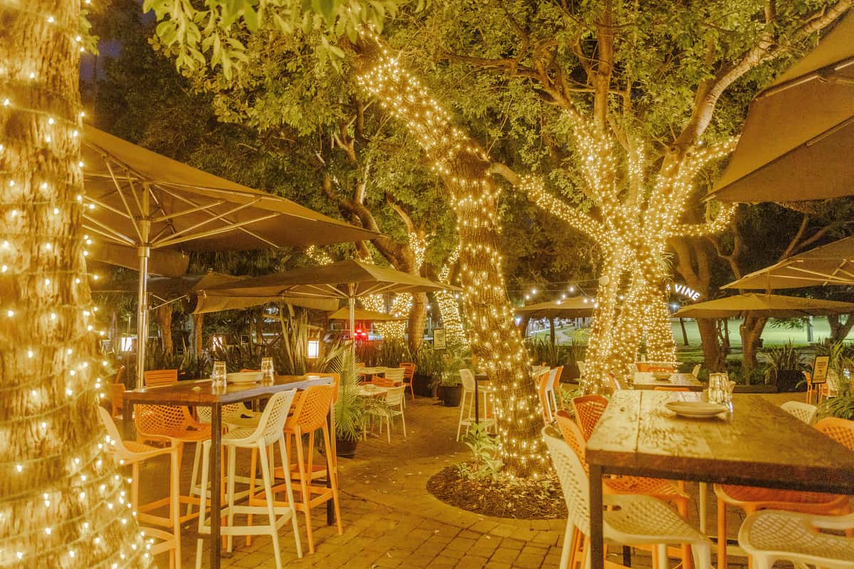 Outdoor anniversary dinner setting with elegant tables, umbrellas, and glowing tree lights creating an intimate atmosphere.