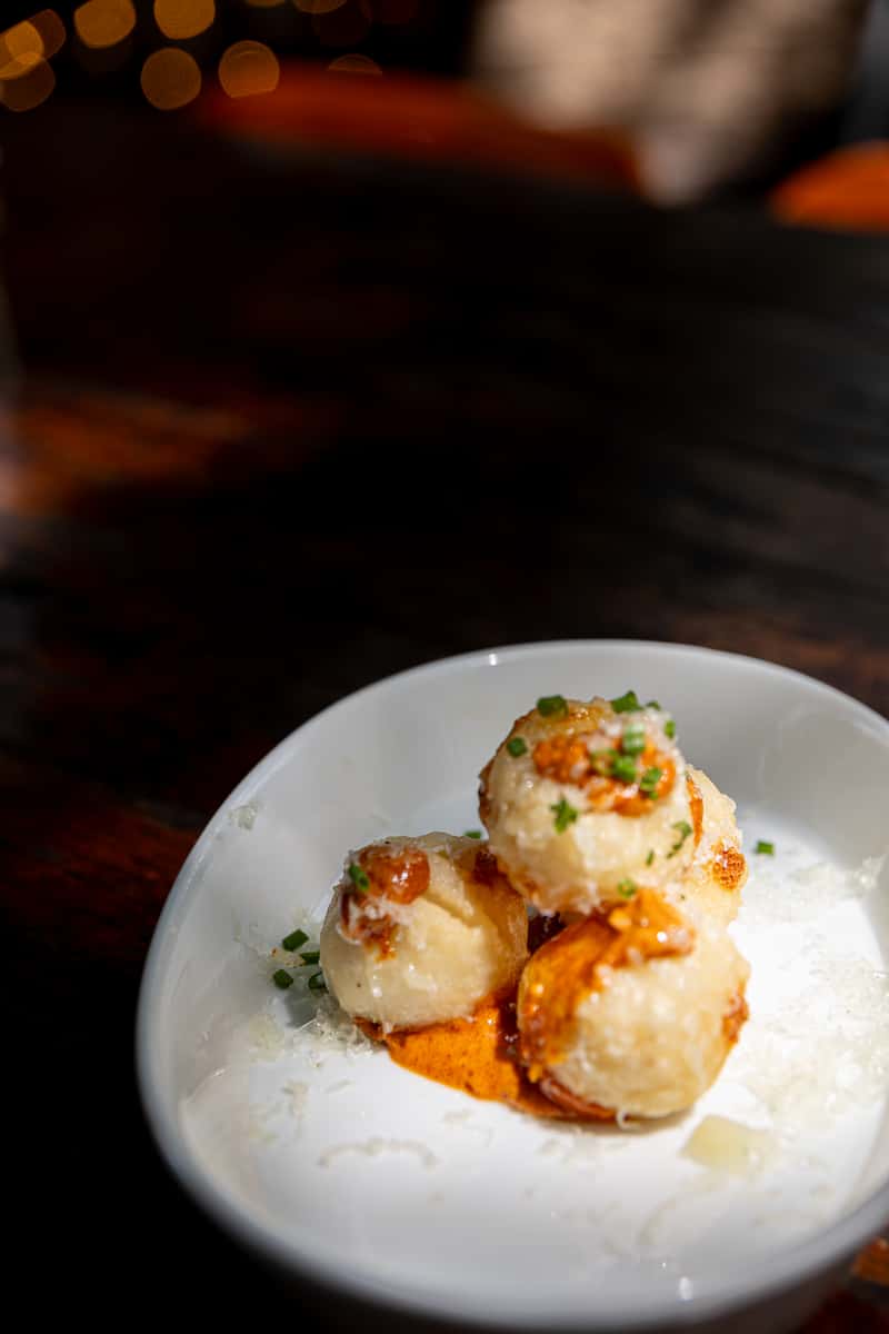 Small plated appetizer with crispy bites, sauce, parmesan, and herbs in a white bowl