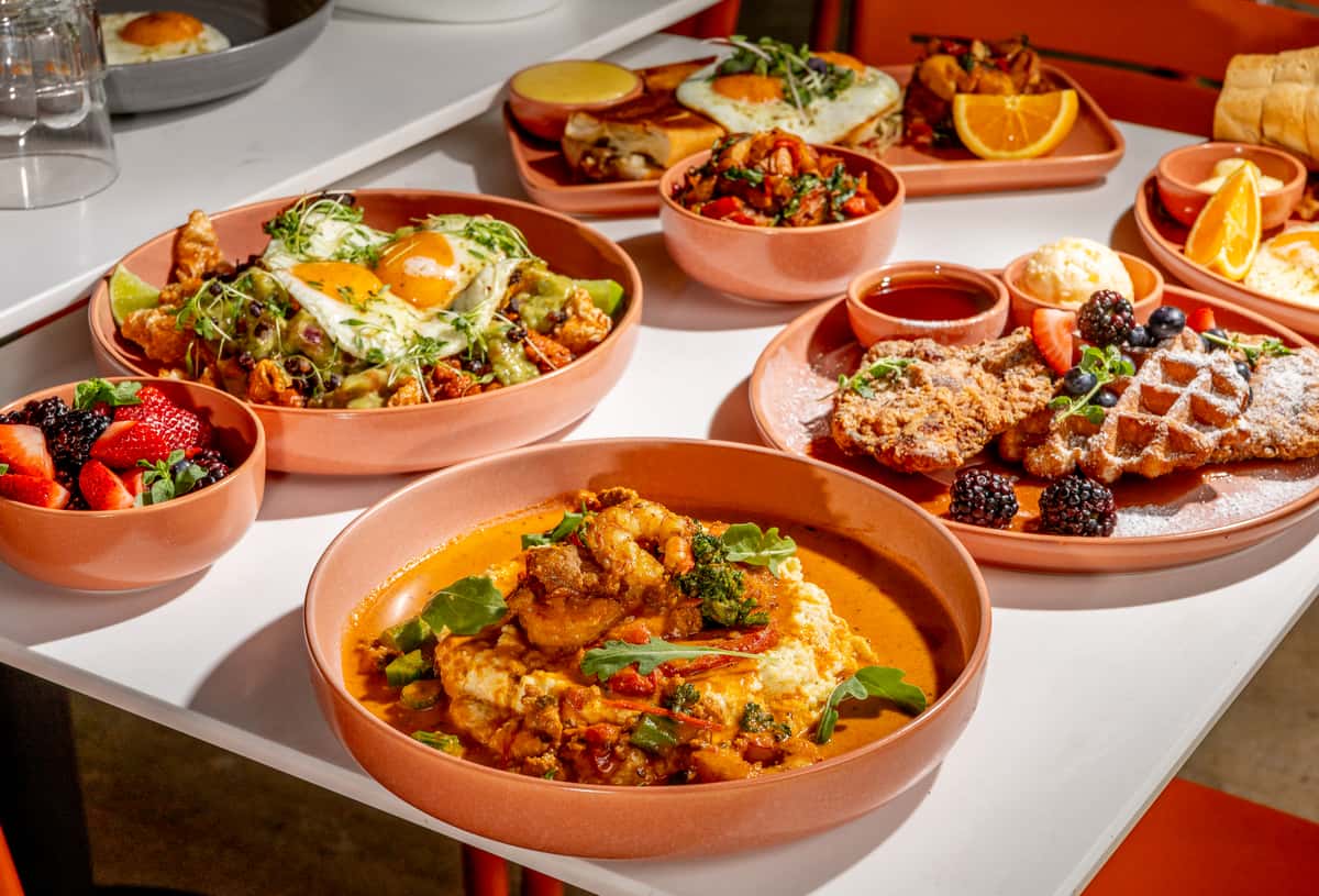 Brunch spread with shrimp and grits, chicken and waffles, eggs, fresh berries, and breakfast plates on a patio table