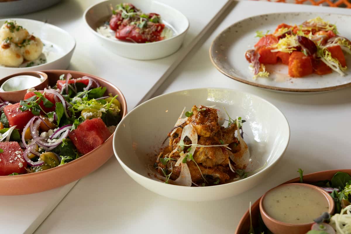 Glass & Vine small plates with watermelon salad, tomatoes, gnocchi, and savory dishes on a white table