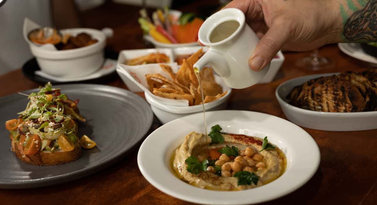 Fresh hummus with olive oil being poured, served with pita chips and Mediterranean dishes at Glass & Vine