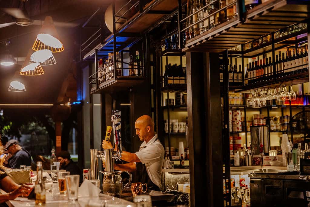 Bartender serving draft beer at an indoor bar with guests seated at the counter and liquor bottles displayed behind.