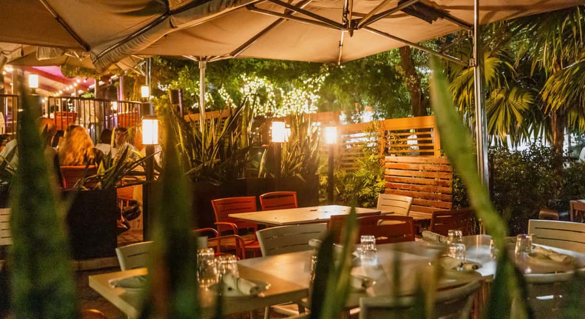 Outdoor restaurant patio with umbrellas, warm lighting, and empty tables set for evening dining.