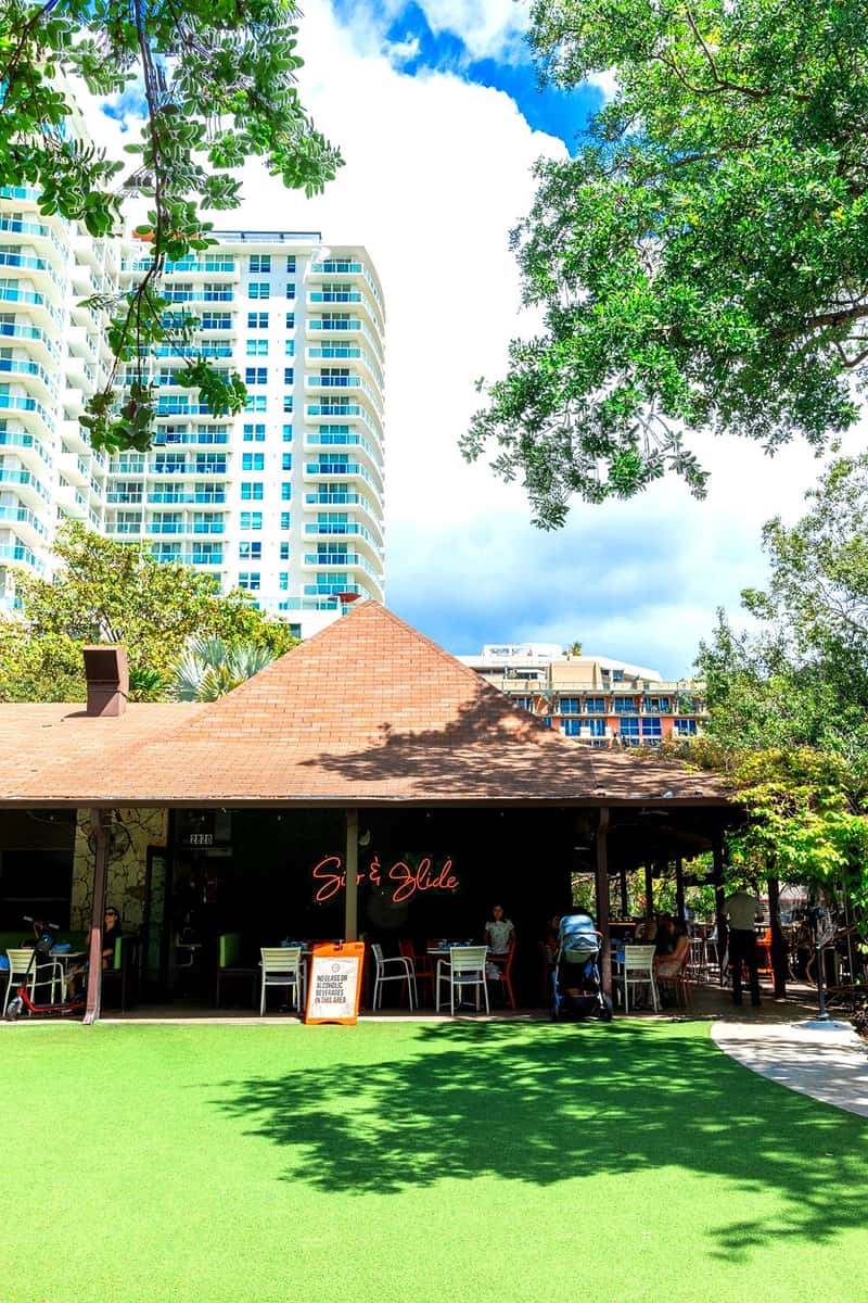 Tropical outdoor venue with shaded dining, green lawn, and surrounding trees