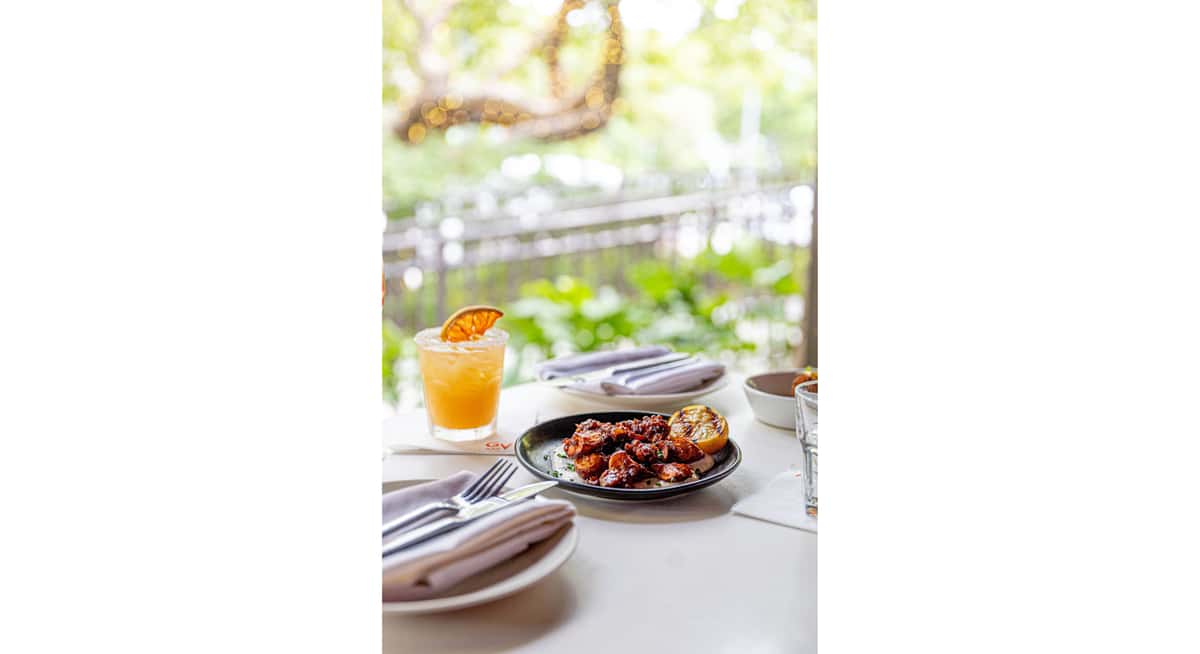Orange cocktail and glazed chicken appetizer on patio table at Glass & Vine in Coconut Grove