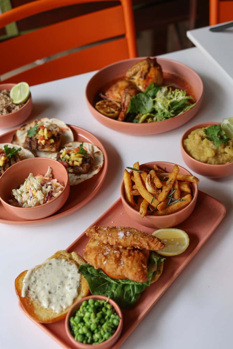 Outdoor table spread with salads, small plates, bread, vegetables, and plated dishes on a restaurant patio