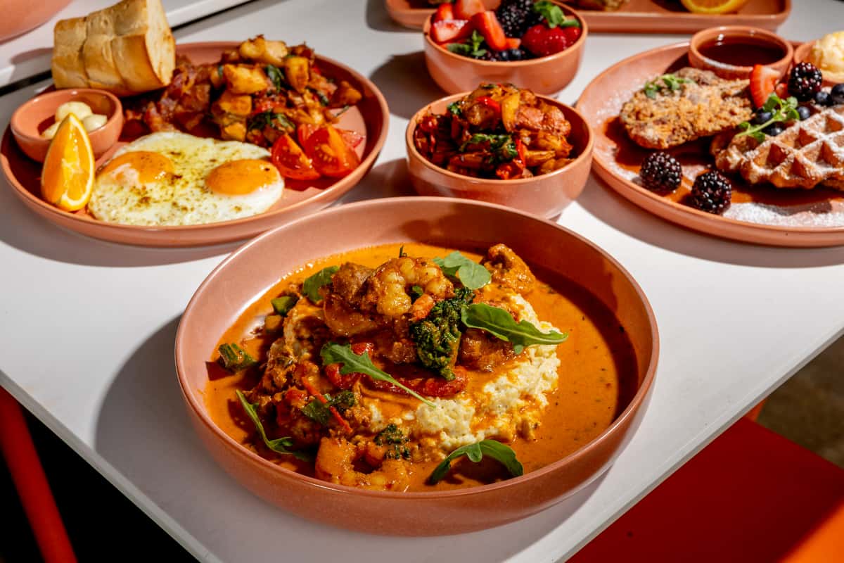 Glass & Vine shrimp and grits with eggs, waffles, berries, and brunch dishes on a white table
