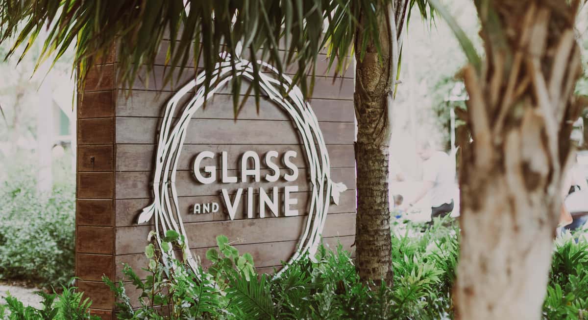 Glass & Vine restaurant sign on wooden wall surrounded by tropical greenery in Coconut Grove.