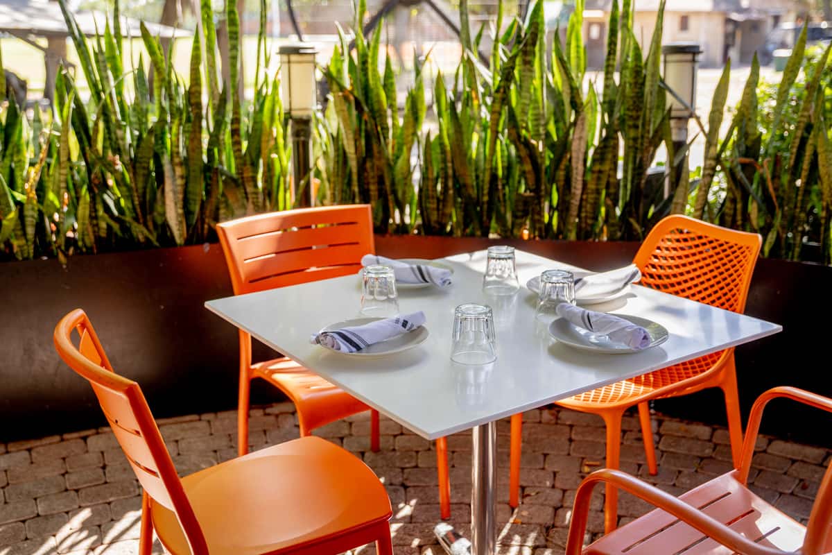 Outdoor Glass and Vine patio table with orange chairs and garden greenery