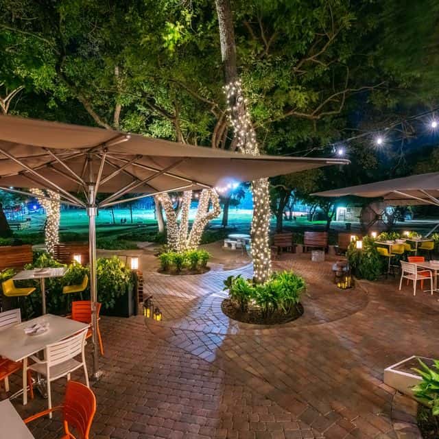 Evening view of Glass & Vine's spacious outdoor dining area in Peacock Park showing wide pathways and accessible table arrangements