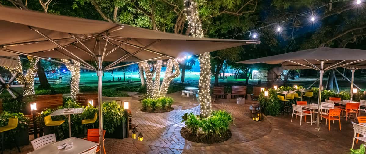 Glass & Vine outdoor dining area with large umbrellas providing shade over tables in a park-like setting
