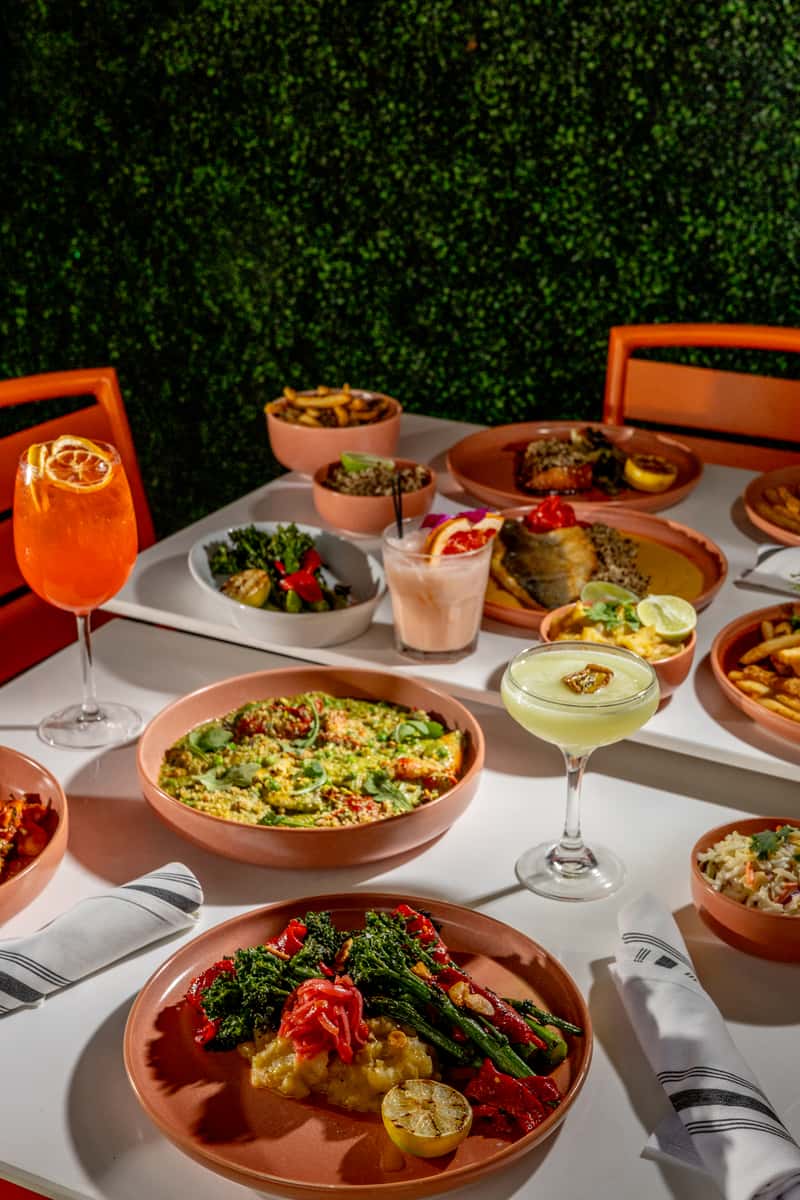 Glass & Vine table with colorful shareable dishes and cocktails against a greenery wall