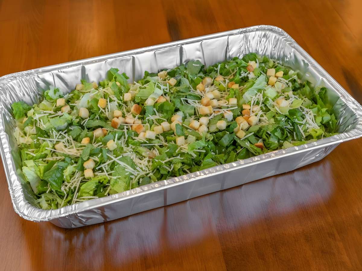 Large catering tray of fresh chopped salad topped with cheese, vegetables, and croutons.