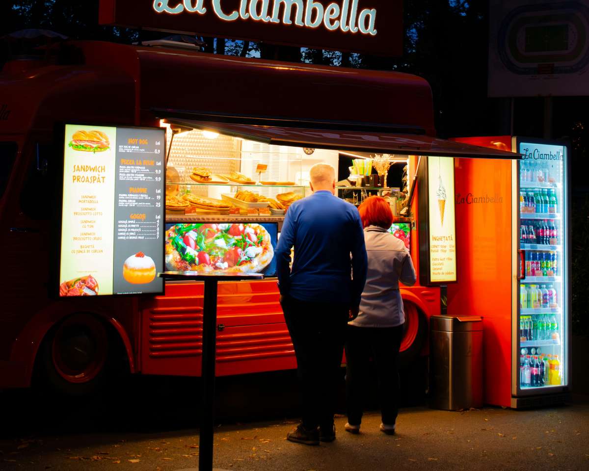 Customers browsing through a large menu outside a food truck at night