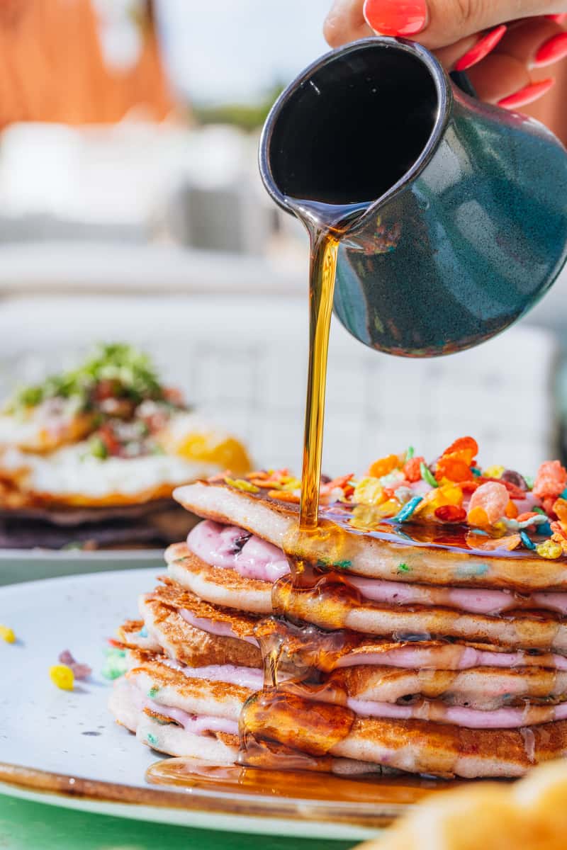 Syrup being poured on a stack of pancakes