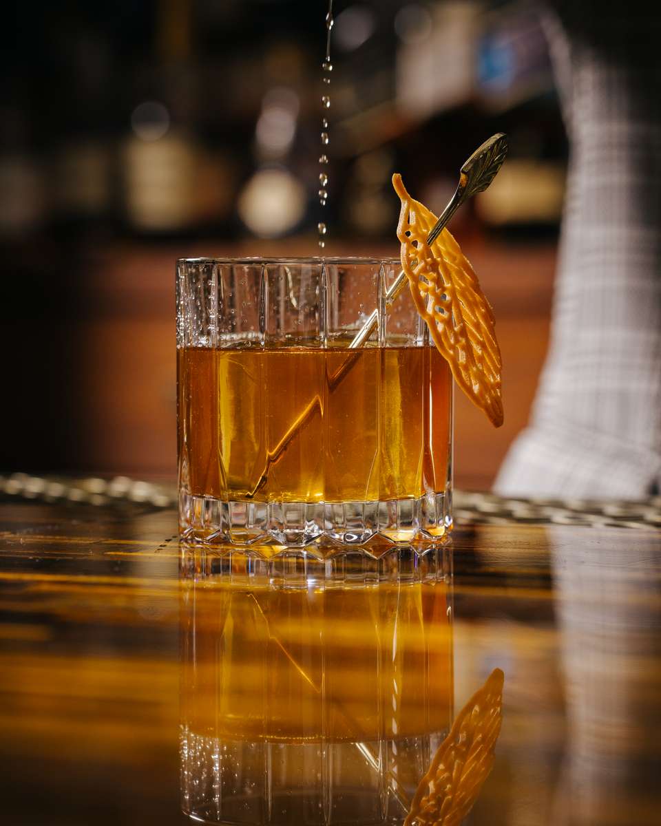 Old fashioned cocktail in a rocks glass with a large ice cube and a citrus peel garnish.