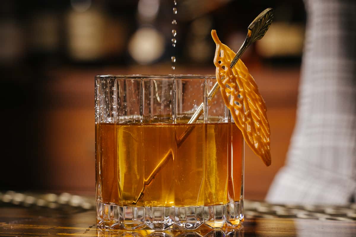 Old fashioned cocktail in a rocks glass with a large ice cube and a citrus peel garnish.