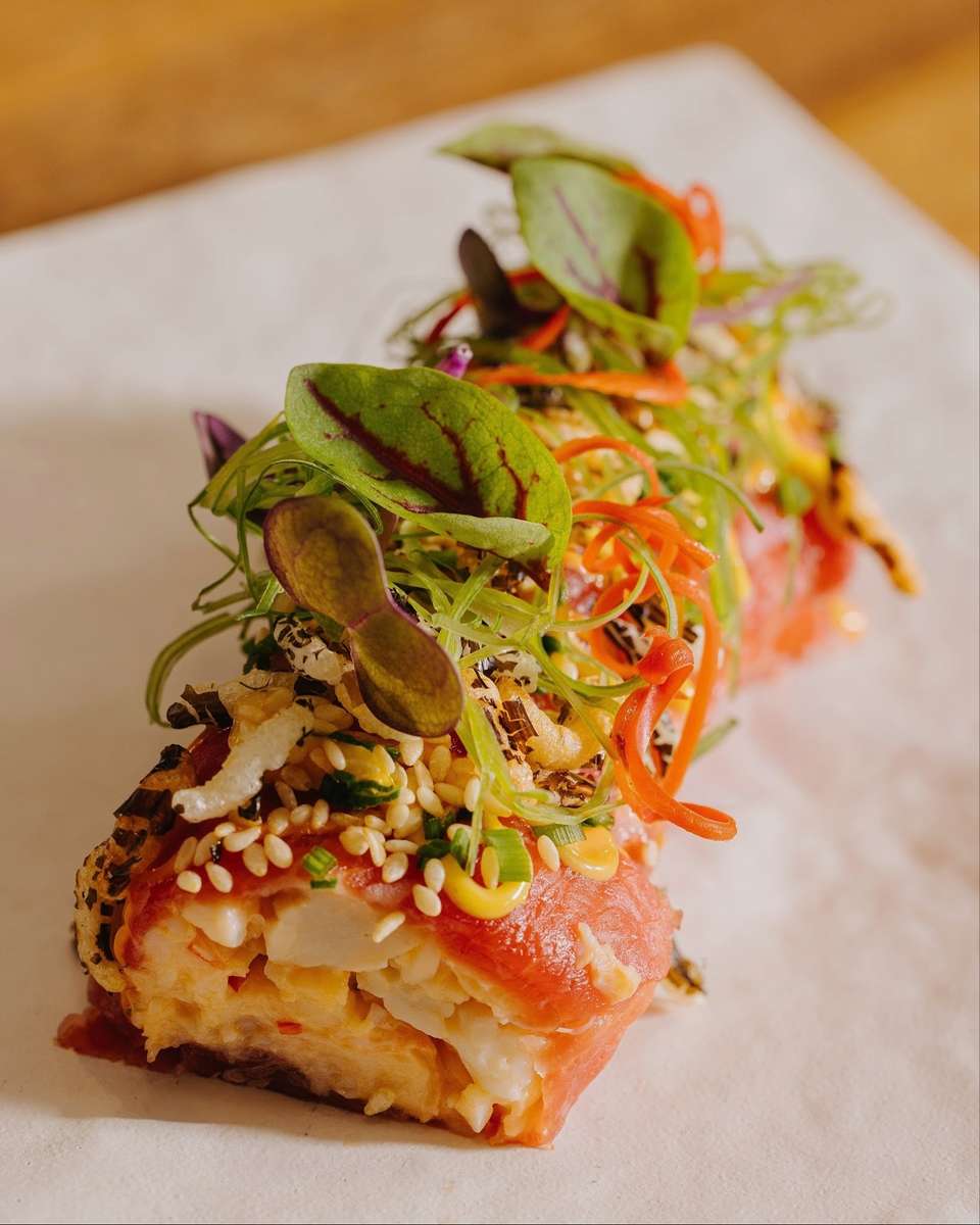 Seared piece of fish topped with microgreens, sliced peppers, and a light sauce on a white plate.