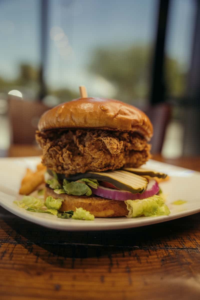 Crispy fried chicken sandwich with lettuce, pickles, red onion, and a toasted brioche bun served with fries on a white plate.